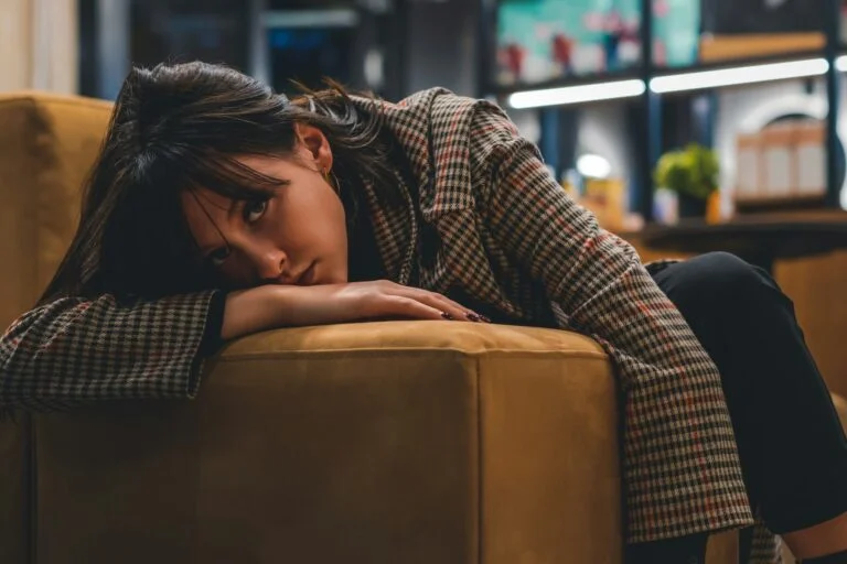 Young woman resting her head on her arms on a sofa, looking worried
