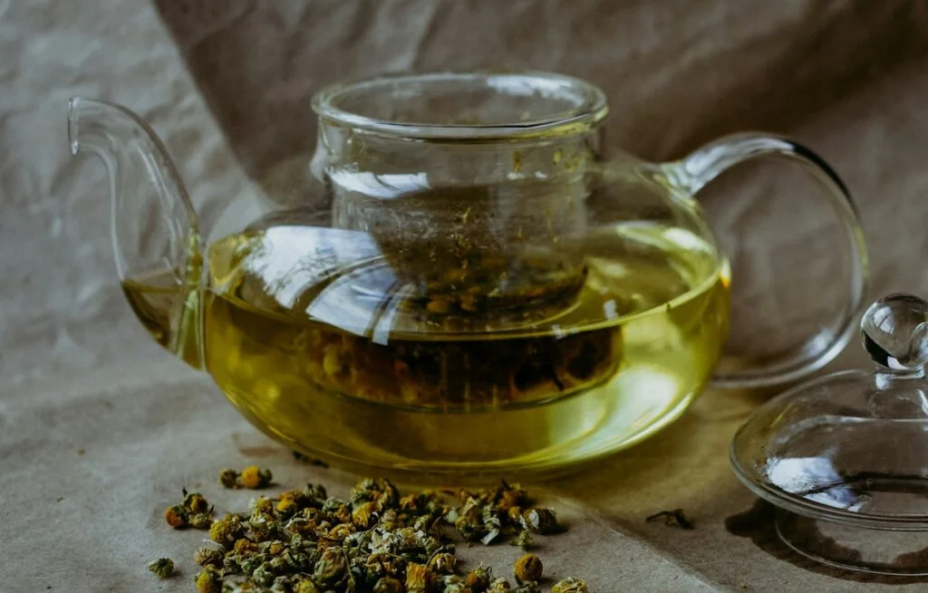 Glass teapot of chamomile tea with dried chamomile flowers