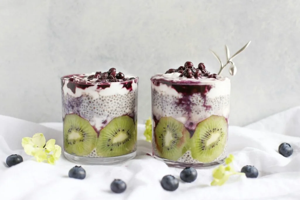 Two glasses of chia seed pudding layered with kiwi, yoghurt and blueberries