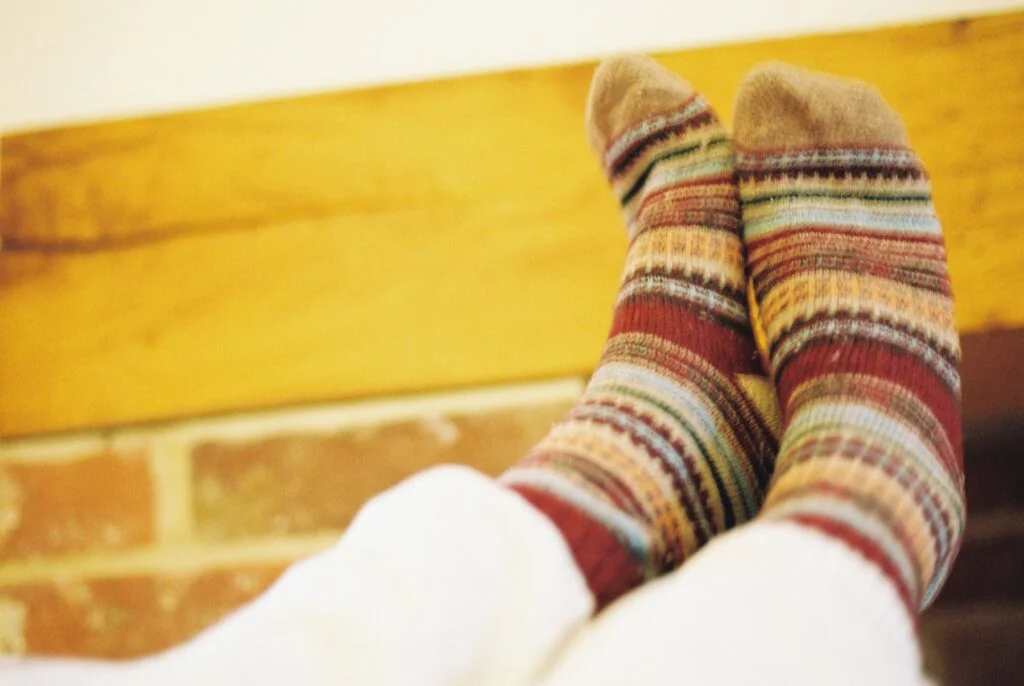 Feet in colourful striped wool socks resting by a warm brick wall