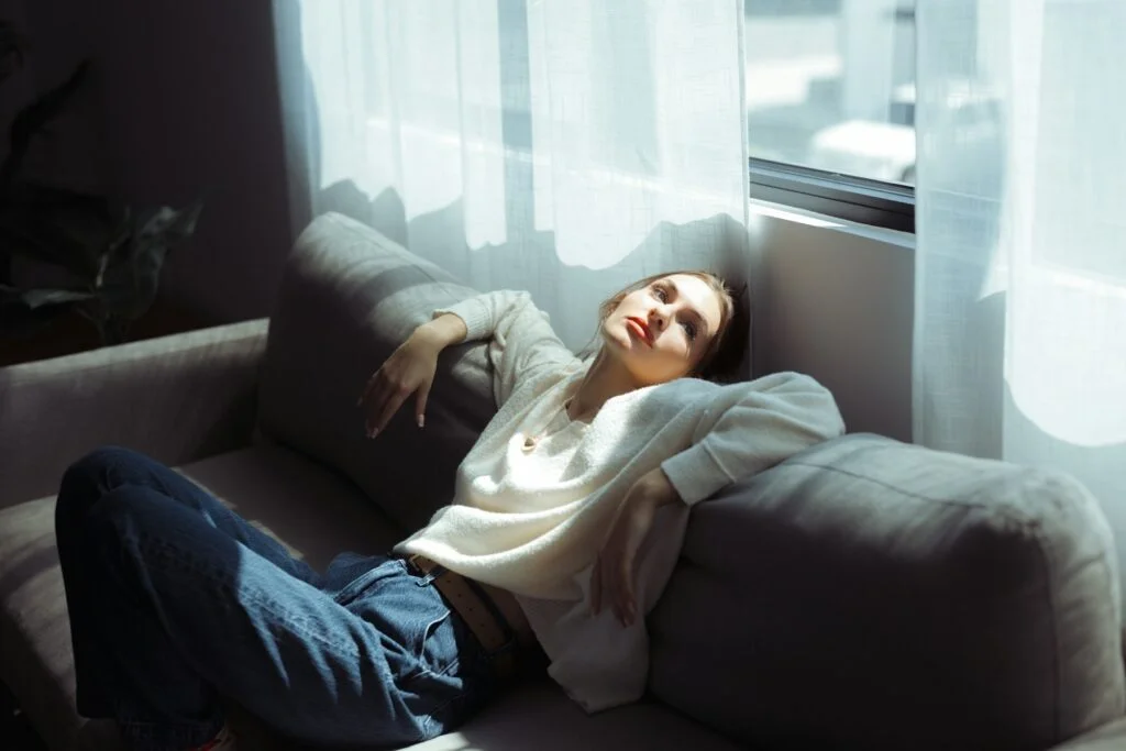 A tired woman resting back on a sofa in soft window light