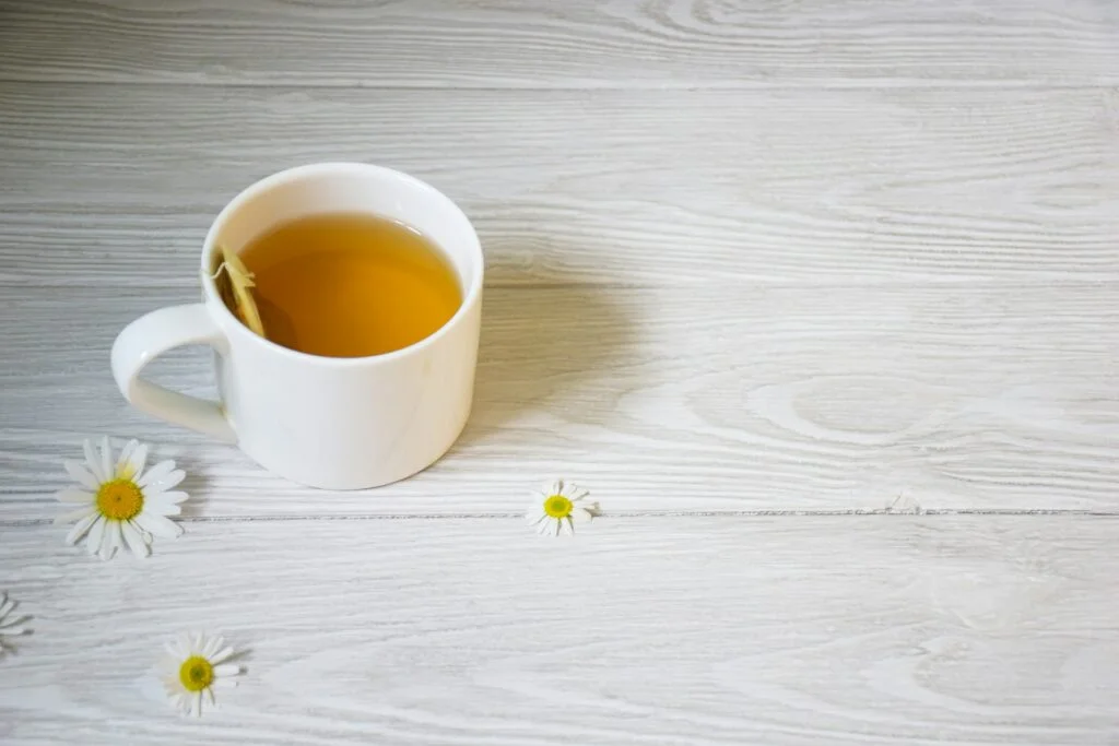 A white mug of camomile tea with daisy flowers on a white table
