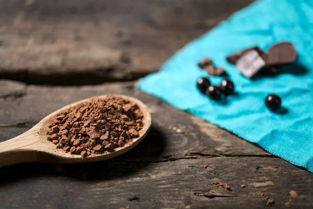 Wooden spoon of cocoa powder on a rustic table with dark chocolate pieces