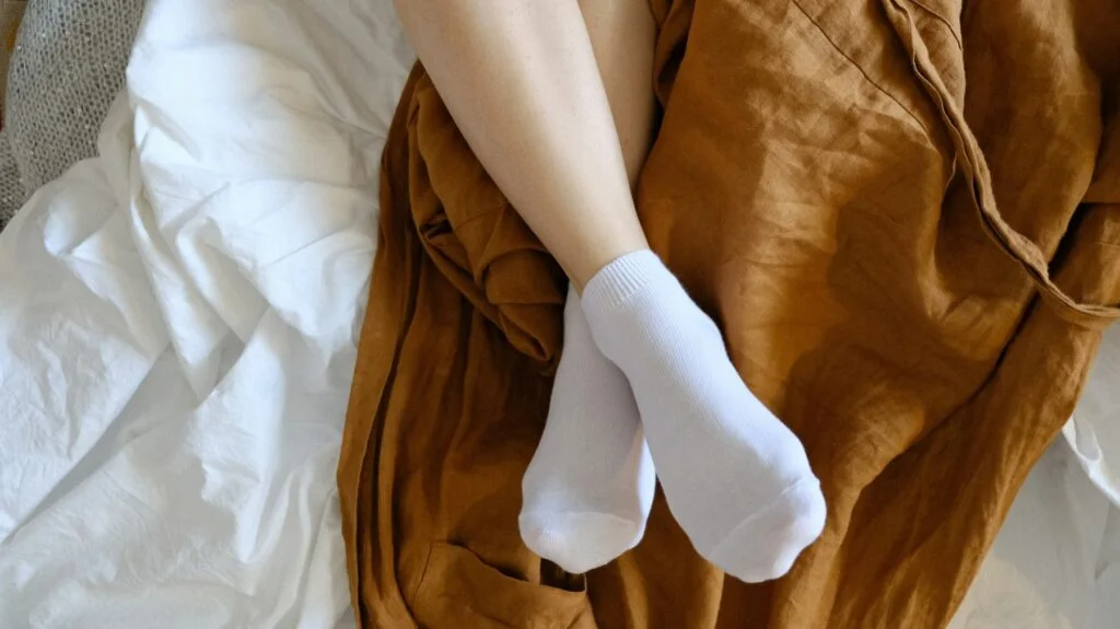 Feet in white socks resting on a bed with a brown linen throw