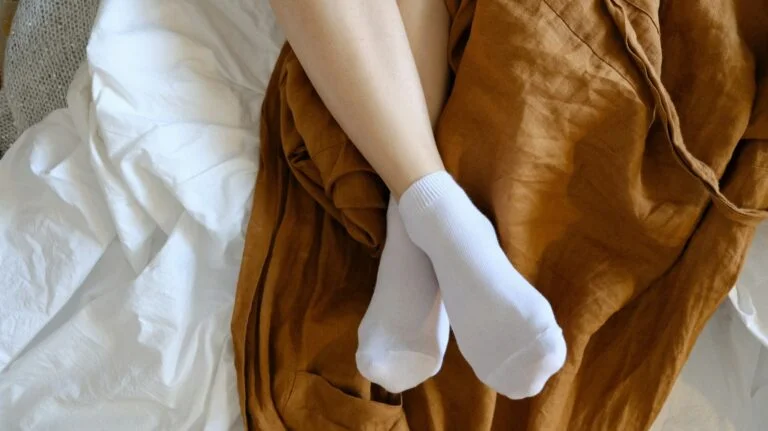 Feet in white socks resting on a bed with a brown linen throw
