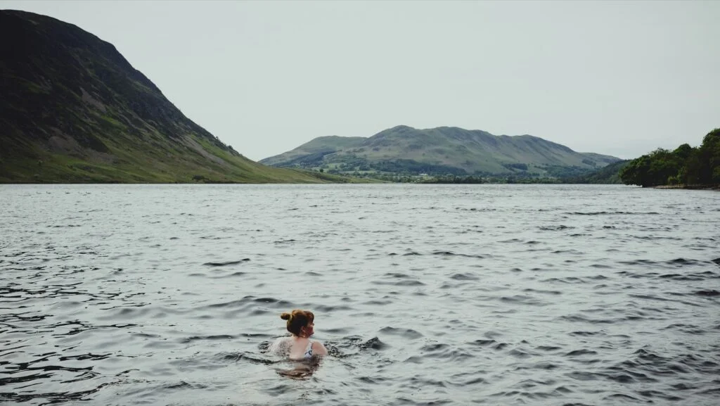 Woman swimming in a cold lake surrounded by hills