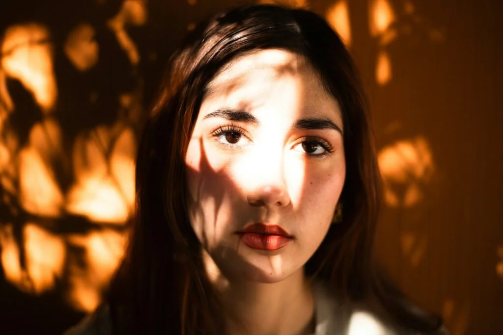A woman's face lit by warm sunlight and leaf shadows