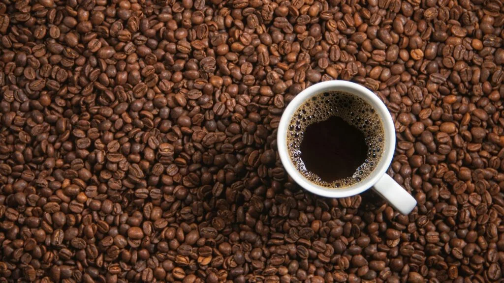 Cup of black coffee on a bed of roasted coffee beans
