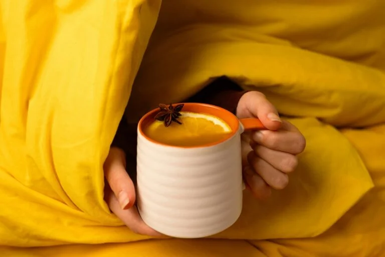 Warm drink in a mug held under a yellow duvet