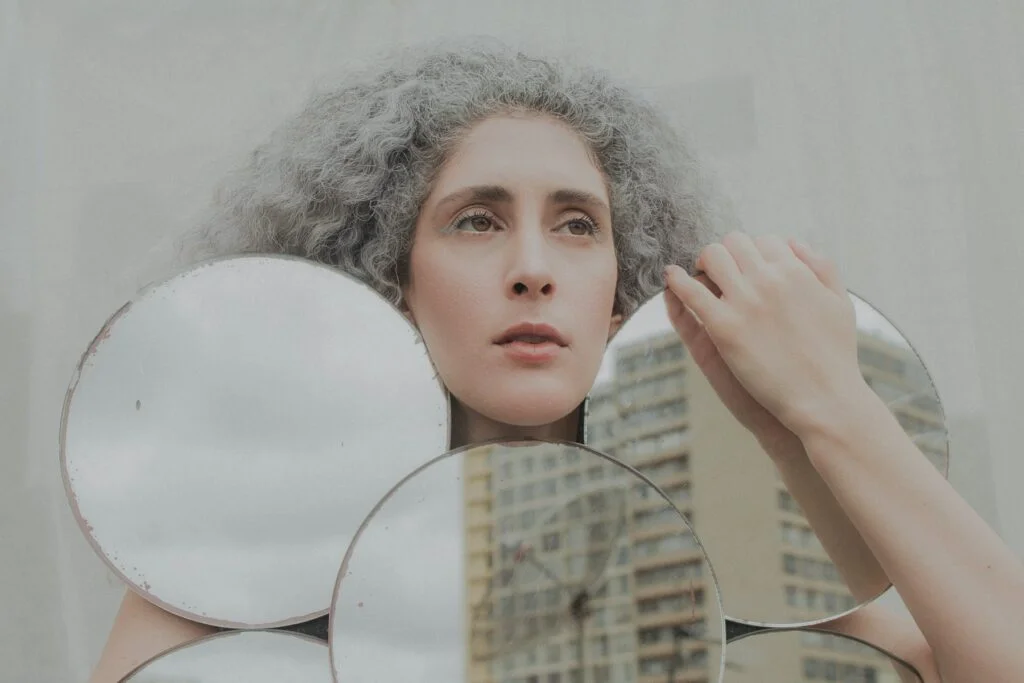 Woman with grey curly hair looking into round mirrors