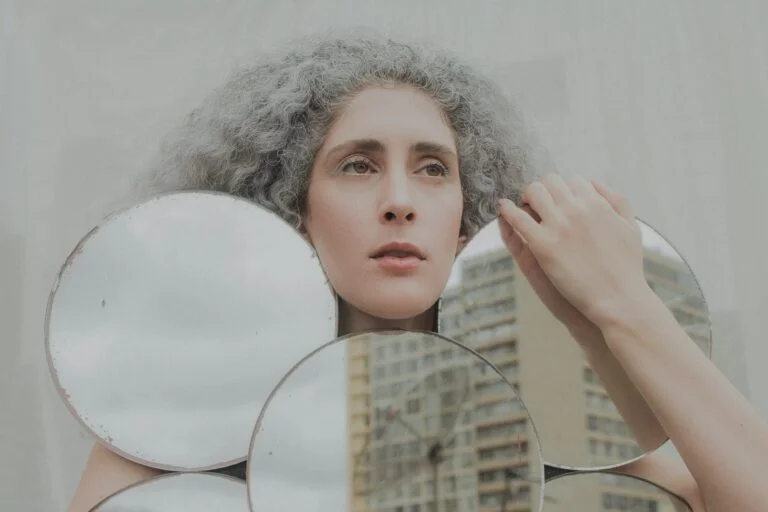 Woman with grey curly hair looking into round mirrors