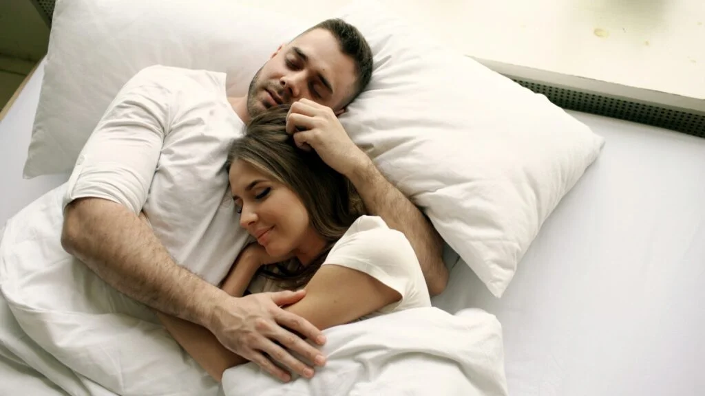 A couple asleep together in a bed with white sheets
