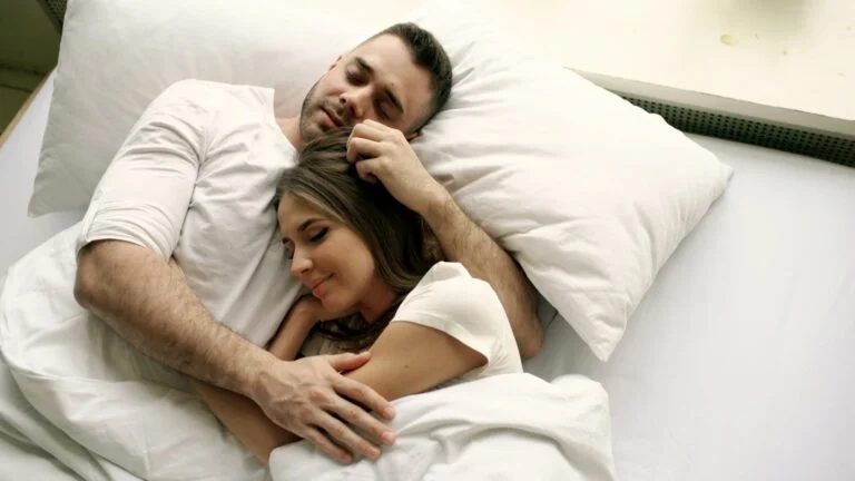 A couple asleep together in a bed with white sheets