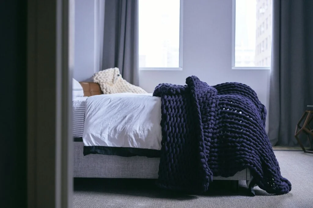 A chunky knitted blanket draped over a made bed in a calm bedroom