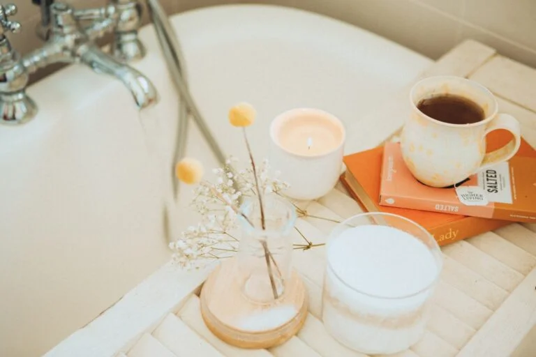 Bath tray with a candle, a warm drink and a jar of bath salts beside a running bath