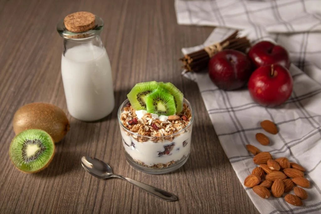 Milk, kiwi, yoghurt with granola, almonds and apples on a table