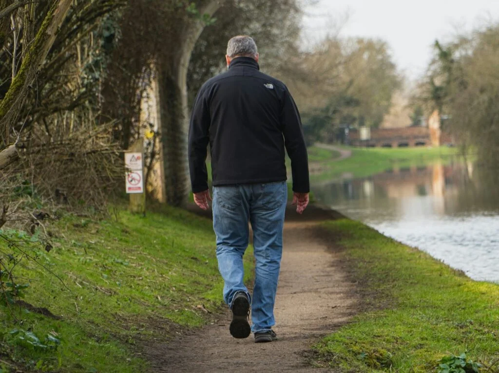 An older man walking along a riverside path