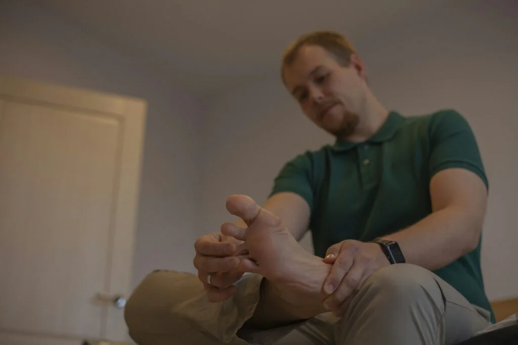 A man sitting down and holding his bare foot near the big toe