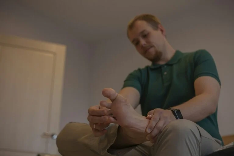 A man sitting down and holding his bare foot near the big toe