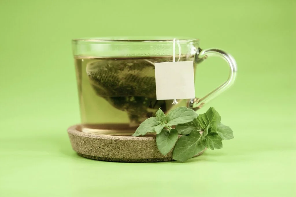 A glass cup of green tea with a tea bag and fresh mint leaves