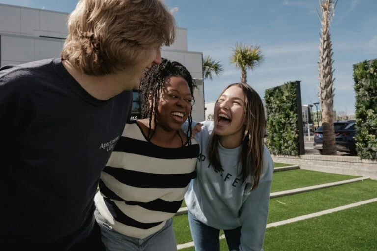 Three friends laughing together outdoors on a sunny day