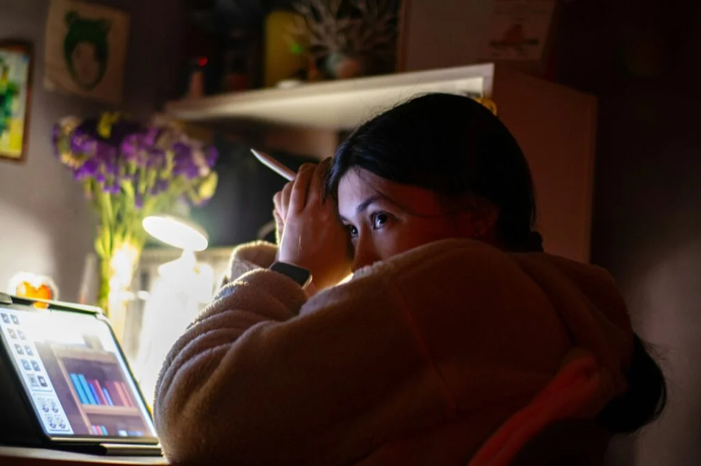 A woman rubbing her forehead while looking at a laptop screen in a dim room