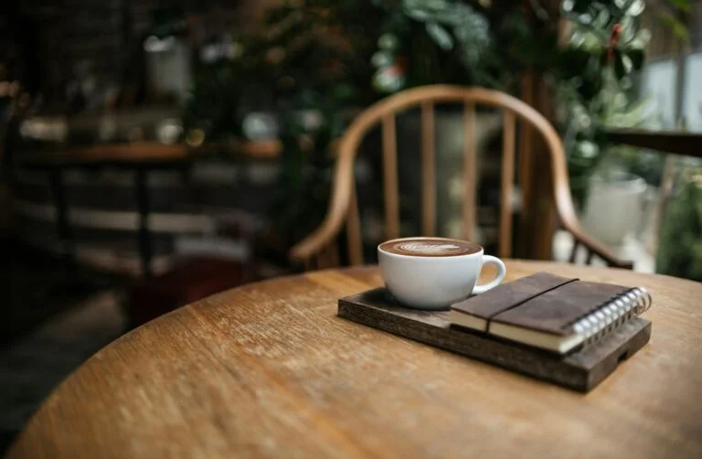 A cup of coffee and a notebook on a wooden café table, ready for planning