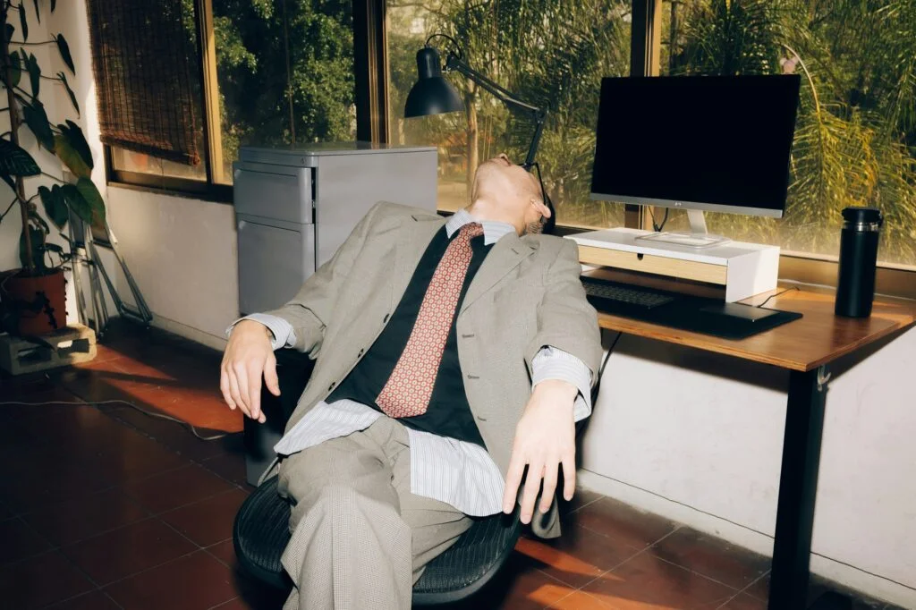 An exhausted man in a suit slumped in his office chair at his desk