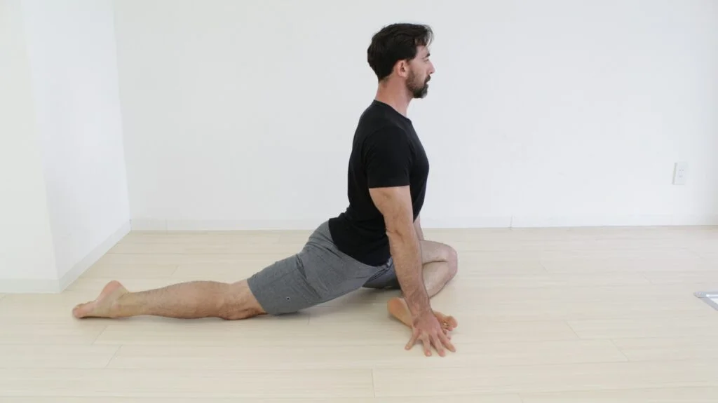 Man doing a pigeon pose hip stretch on a wooden floor