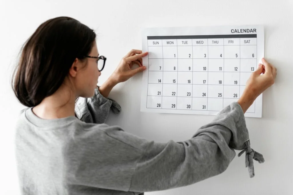 A woman pinning up a monthly calendar on a wall