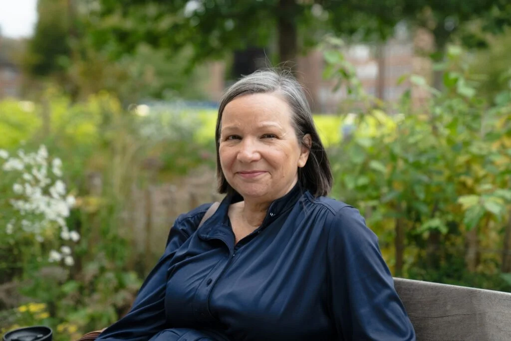 A smiling woman in her fifties sitting on a bench in a garden