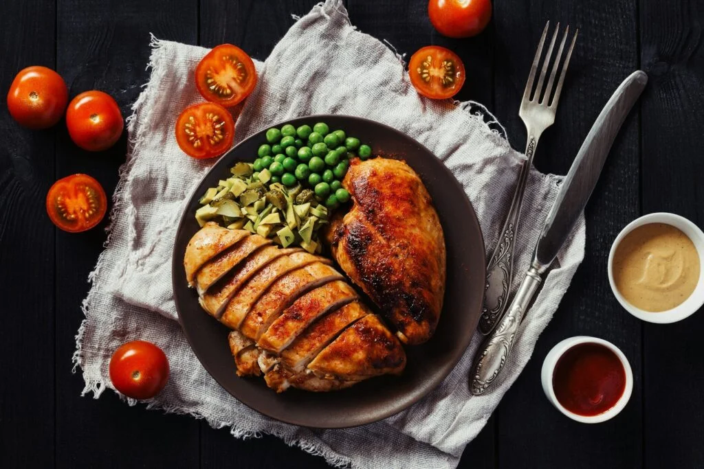 Grilled chicken breast with peas and tomatoes on a dark plate, a high-protein meal