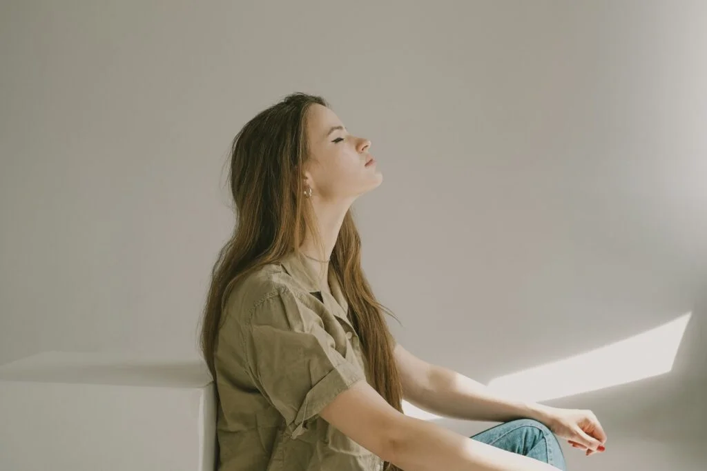 A woman sitting with her eyes closed and her face turned up towards soft sunlight