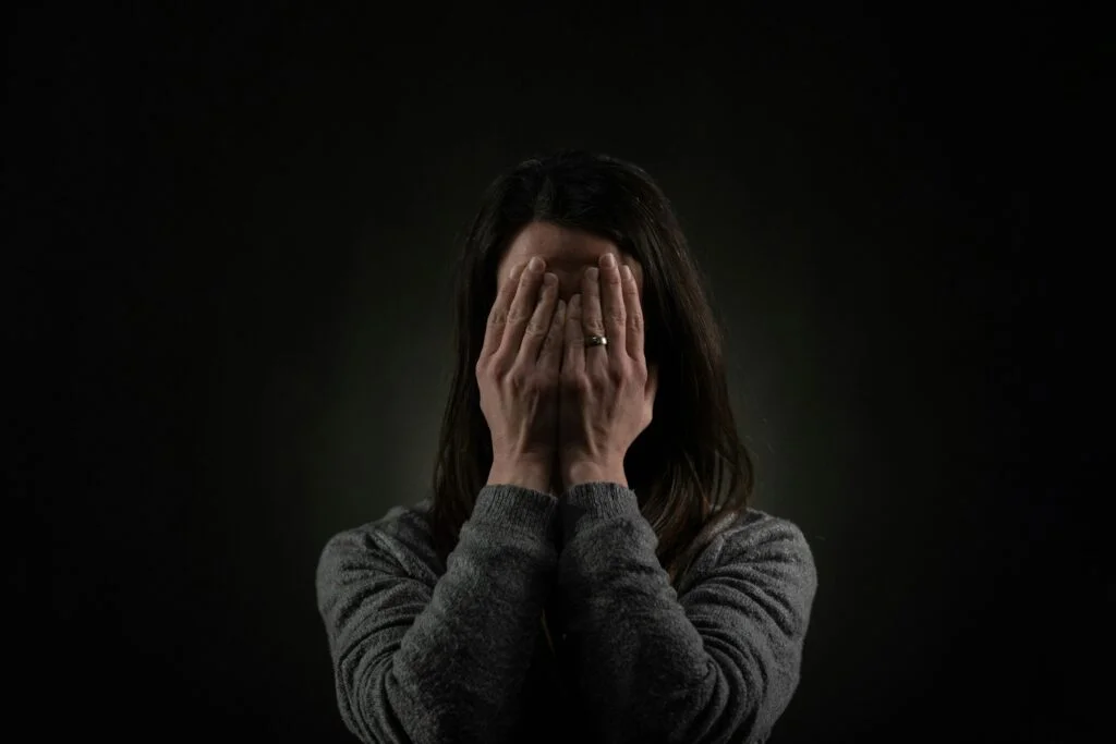 A woman covering her face with her hands against a dark background
