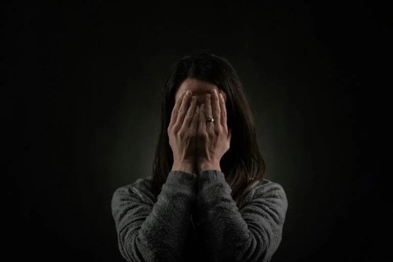 A woman covering her face with her hands against a dark background