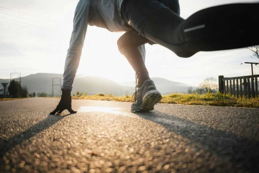 A runner crouched at the start of a country road at sunrise