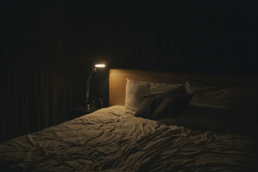 A dimly lit bedroom with a bedside lamp next to an unmade bed