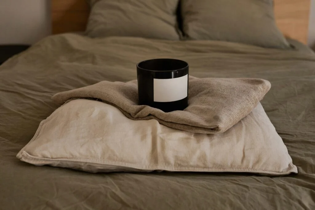A candle on a folded blanket and linen pillow on a cosy bed