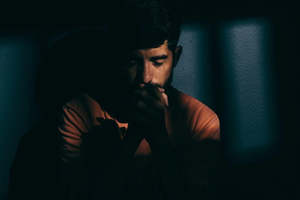 A man deep in thought with his hands to his face in a dark room