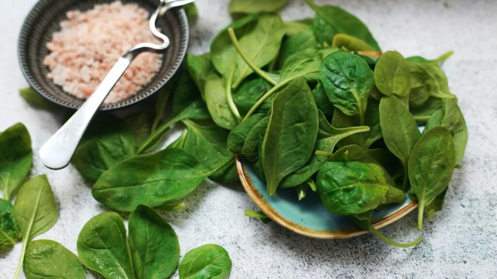 Fresh spinach leaves in a bowl beside a dish of salt
