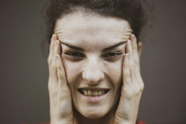 A woman pressing her hands to the sides of her face with her teeth clenched