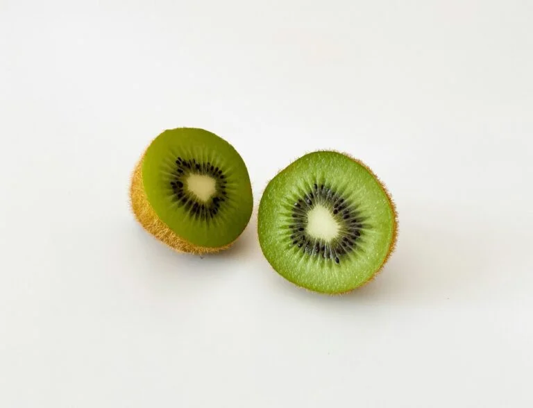 A green kiwi fruit cut in half on a white surface