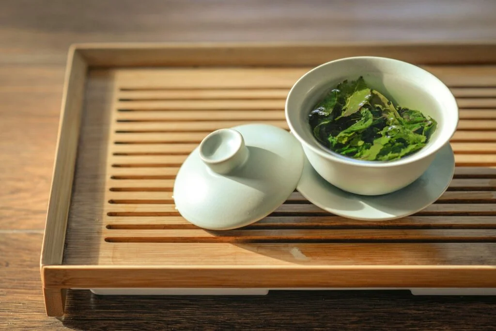 Green tea leaves in a white bowl on a wooden tea tray