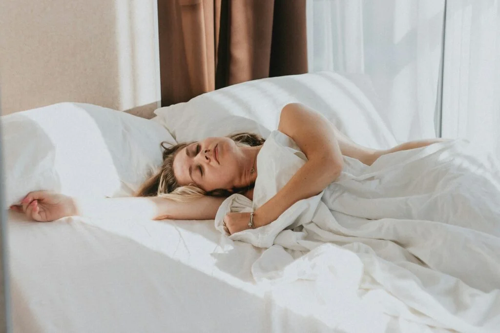 A woman asleep in a bright bedroom with morning light coming through the curtains