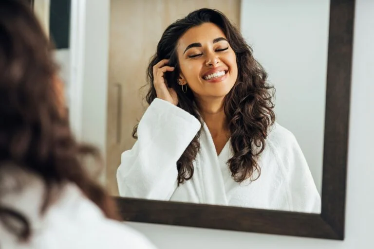 A smiling woman in a bathrobe looking at her reflection in a mirror