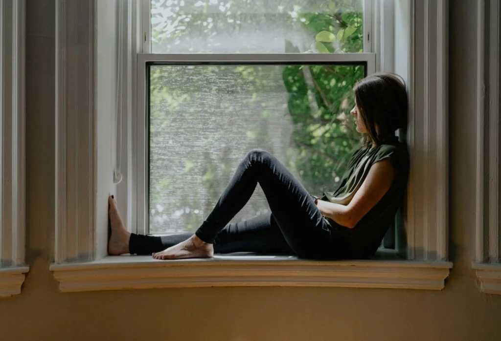 Woman sitting quietly on a window sill, looking out