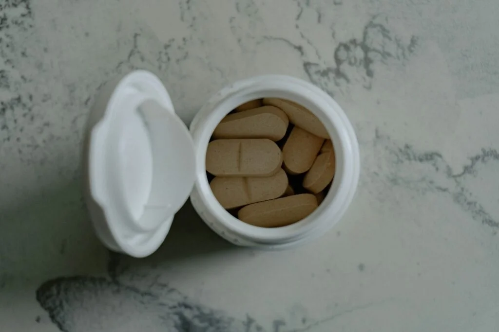 Open bottle of supplement tablets on a marble surface