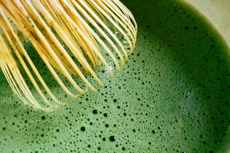 Bamboo whisk frothing bright green matcha tea in a bowl