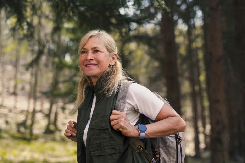A smiling woman in her fifties walking in a forest with a backpack