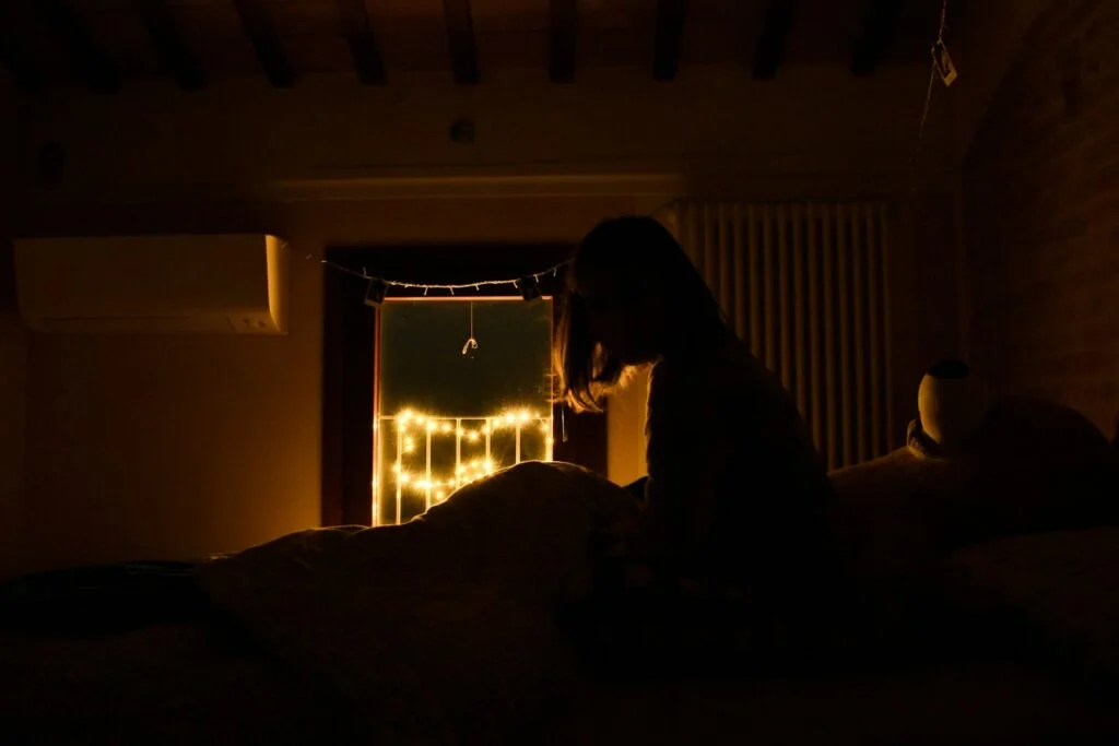 A person sitting up in bed in a dark bedroom at night, awake and unable to get back to sleep